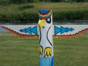 Red, blue, gold and white painted eagle made from a wooden pole with beak and wings extended.