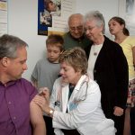 A nurse administering a vaccine while a line of people wait their turn.