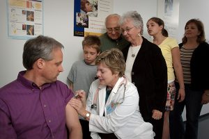 A nurse administering a vaccine while a line of people wait their turn.