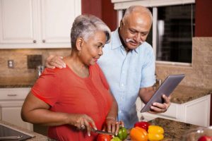 Man and woman reading a recipe from a tablet while she cuts vegetables.