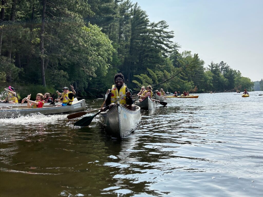 Youth participants sit in a canoe and smile for the camera