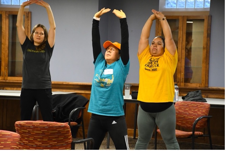 Two participants and a volunteer leader stretch their hands above their heads.