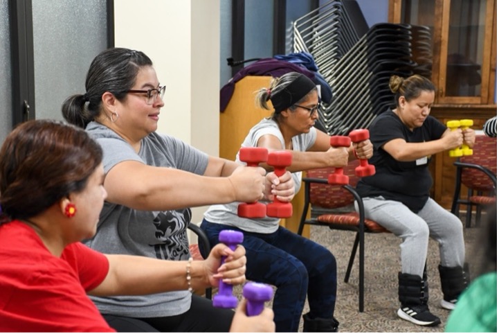 Four seated GenteFuerte participants deeply focused on holding their weights in front of them.