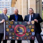 Three graduates hold the Command College flag displaying patches from each department represented