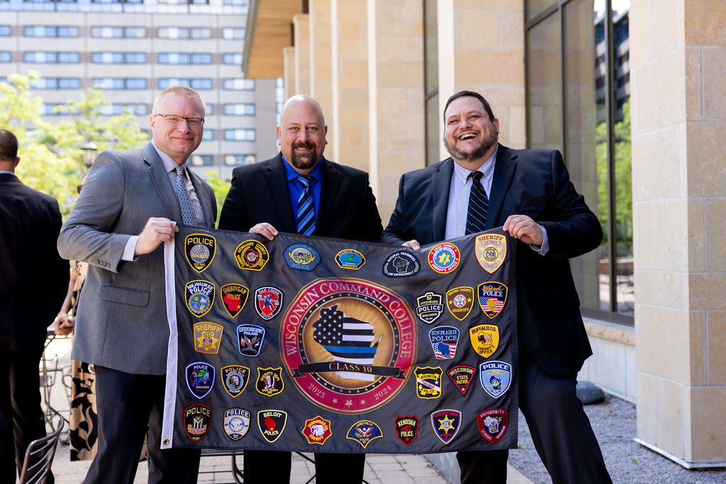 Three Command College graduates hold flag displaying patches from police departments