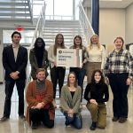 Group of AmeriCorps members hold sign that says "Serving Here"