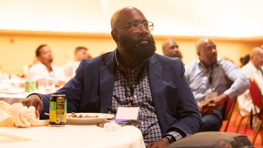 A father listens with other conference attendees to a keynote speaker during lunch.