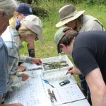Several people lean over documents and maps