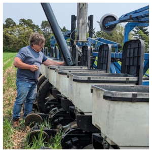 Man stands in a field near a planter,  looking in the bins.