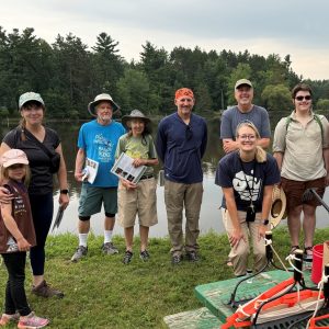 Group of people holding clip boards pose for a photo beside a river