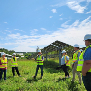 People stand outside near large solar panel in hard hats and reflective vests