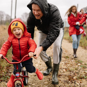 Man in jacket pushes laughing child in coat and hat on a tricycle