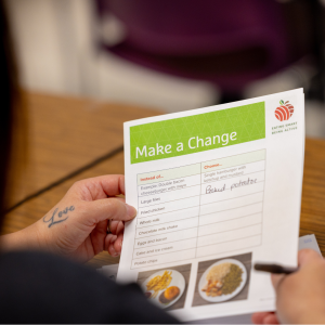 Hands holding piece of paper that says "Make a change" with chart to fill in names of food