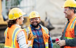 Two employees in hard hats and reflective vests stand at a construction site 