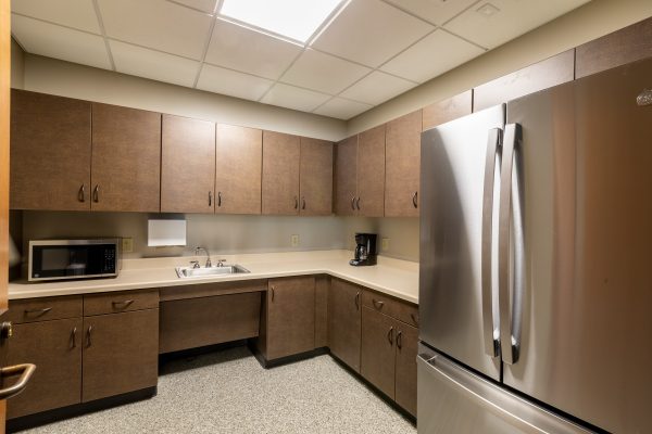 This small kitchen has dark brown cabinets above and below a tan counter. Appliances include a microwave, refrigerator and a coffee pot.