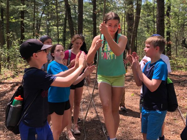 This image shows a teambuilding activity where a youth holding onto a rope is being supported by her teammates. 
