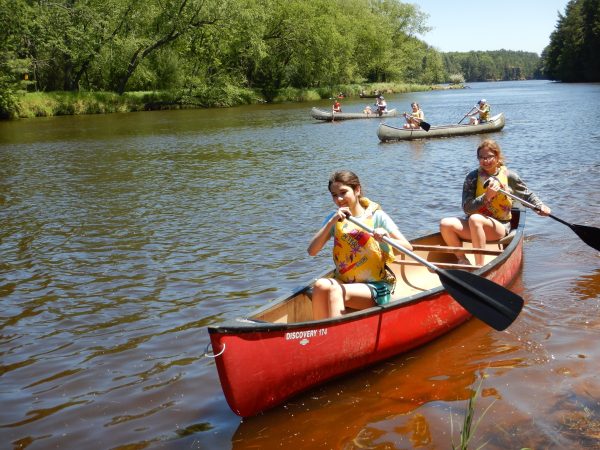 Youth canoeing in a red boat up river towards the camera