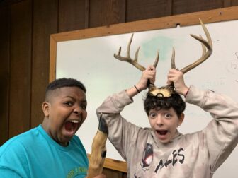 Two youth smile at the camera while holding deer antlers